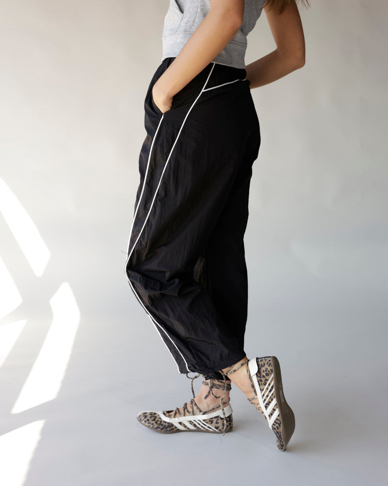 Black windbreaker pants with white contrast piping, worn with leopard print sneakers