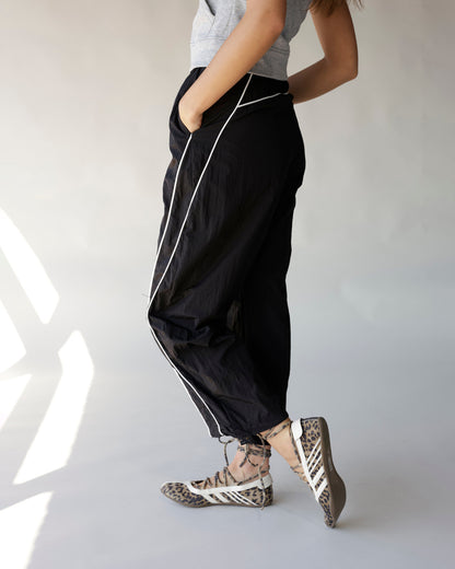 Black windbreaker pants with white contrast piping, worn with leopard print sneakers