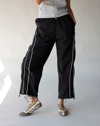 Black windbreaker pants with white side stripes, elastic waist, and adjustable hem