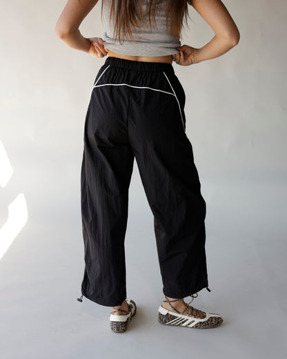 Black windbreaker pants with white contrast piping, elastic waist, and adjustable hem drawcords