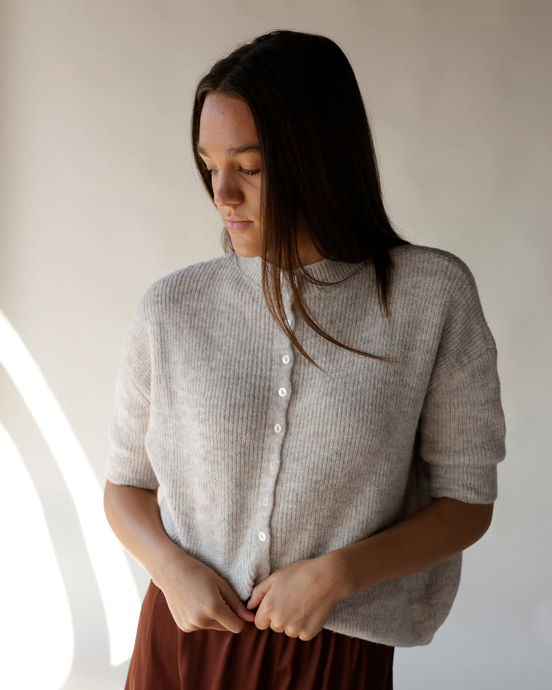 Gray short-sleeve ribbed knit cardigan with white buttons, worn by a model