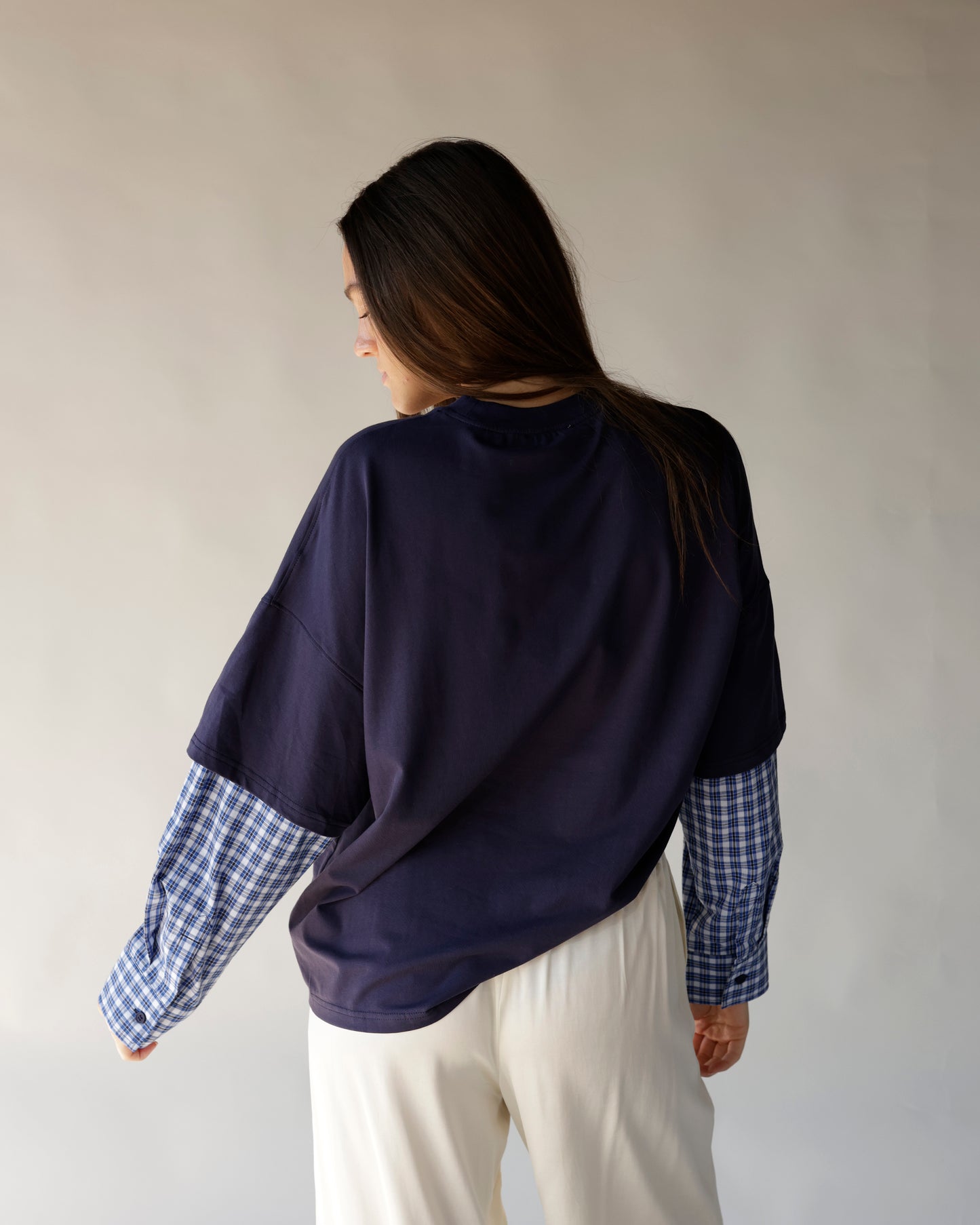 Oversized navy tee with blue plaid shirt sleeves, worn with cream trousers