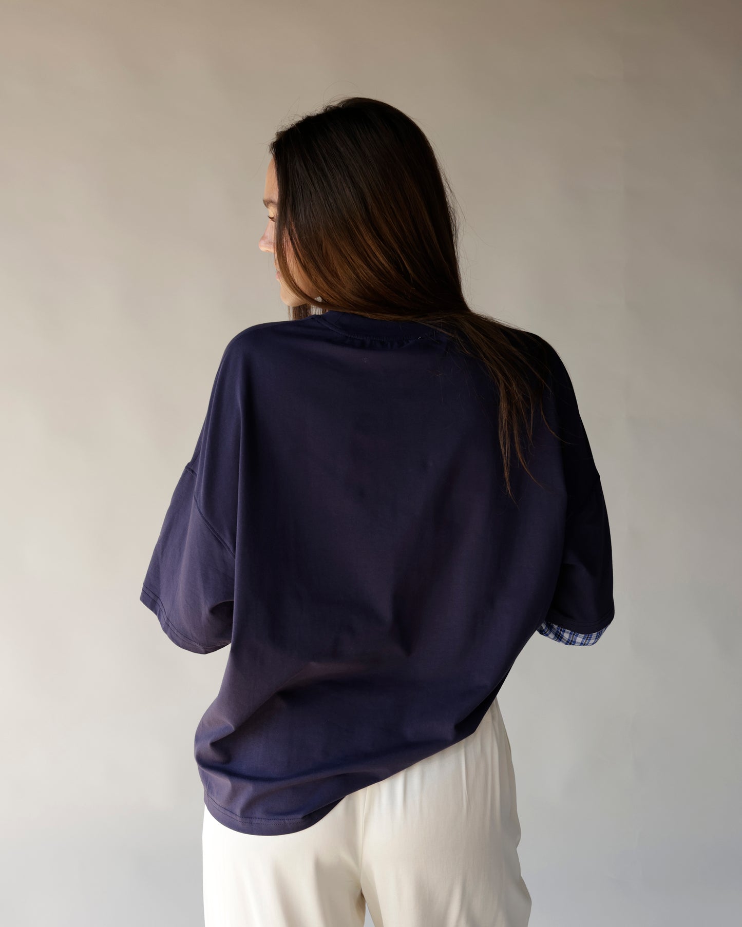 Oversized navy tee with plaid sleeve cuffs, worn with white pants, back view.