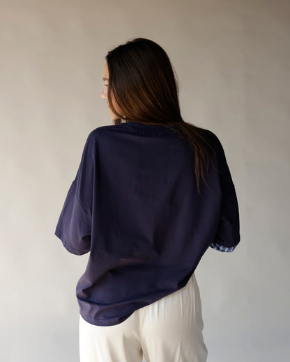 Oversized navy tee with plaid sleeve cuffs, worn with white pants, back view.