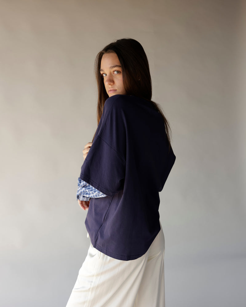 Women's navy oversized top layered over blue plaid shirt with white skirt