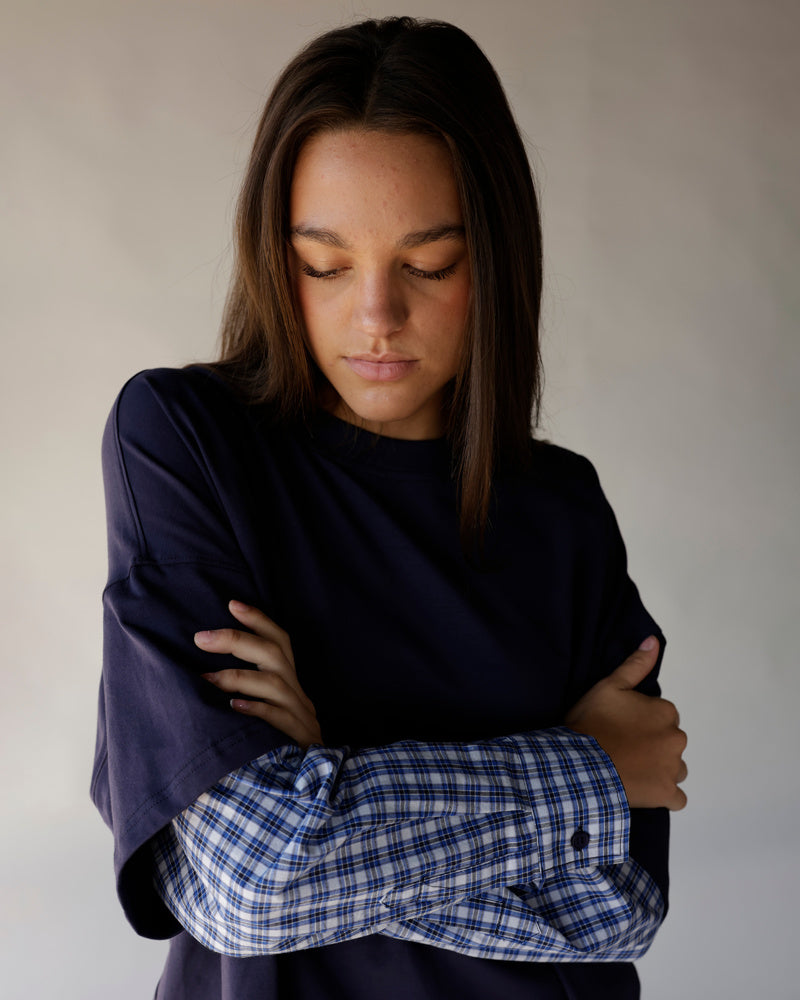 Woman wearing navy oversized top with blue plaid flannel layered sleeves, arms crossed
