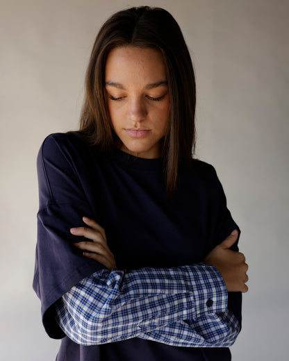 Woman wearing navy oversized top with blue plaid flannel layered sleeves, arms crossed