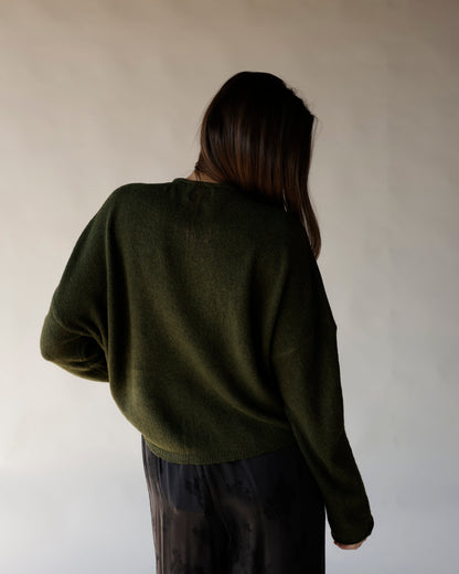 Dark olive green oversized knit sweater, back view, worn with dark satin skirt