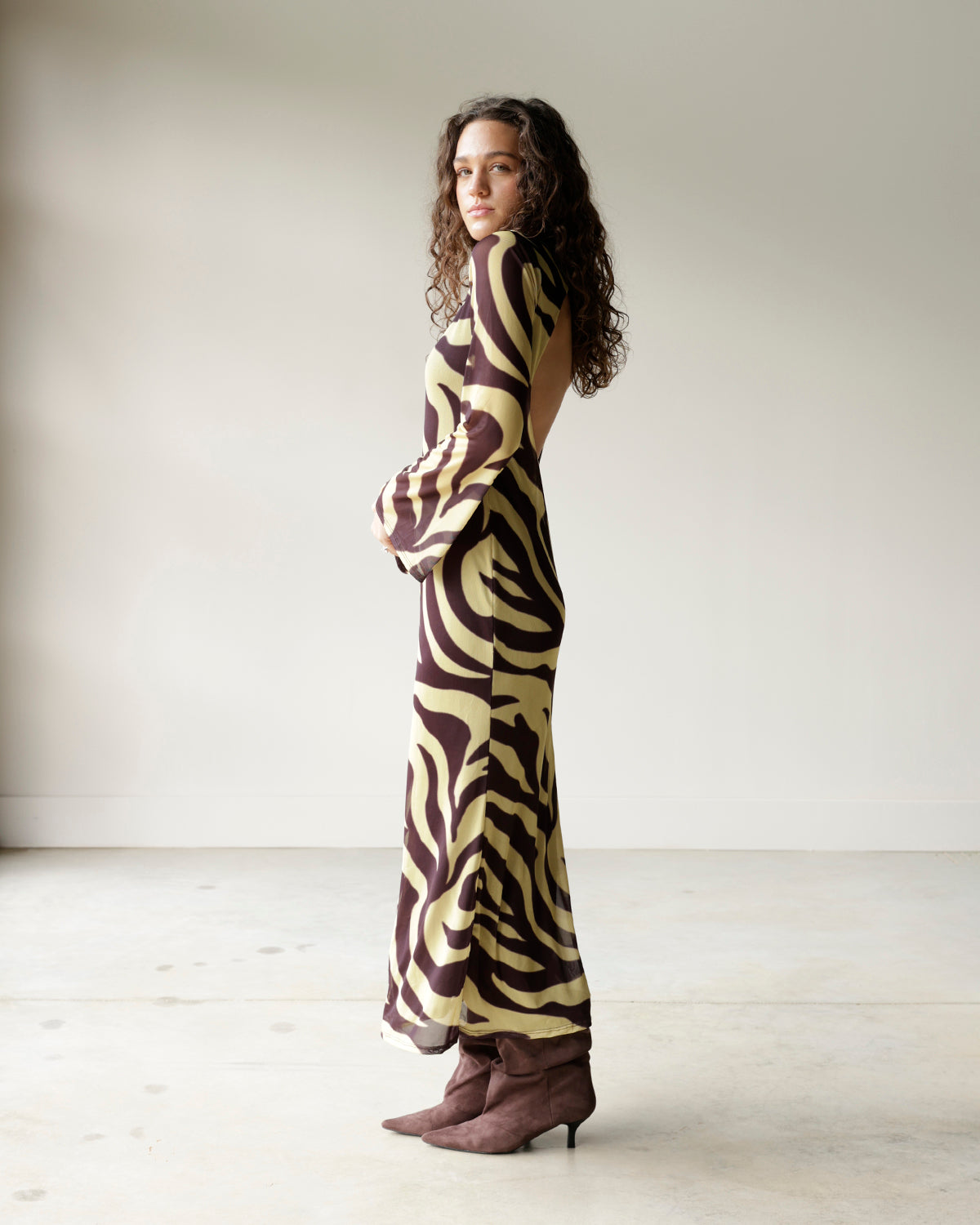 woman wearing an emory park chocolate brown and yellow zebra print maxi dress with long flared sleeves, round neckline and dramatic open back.