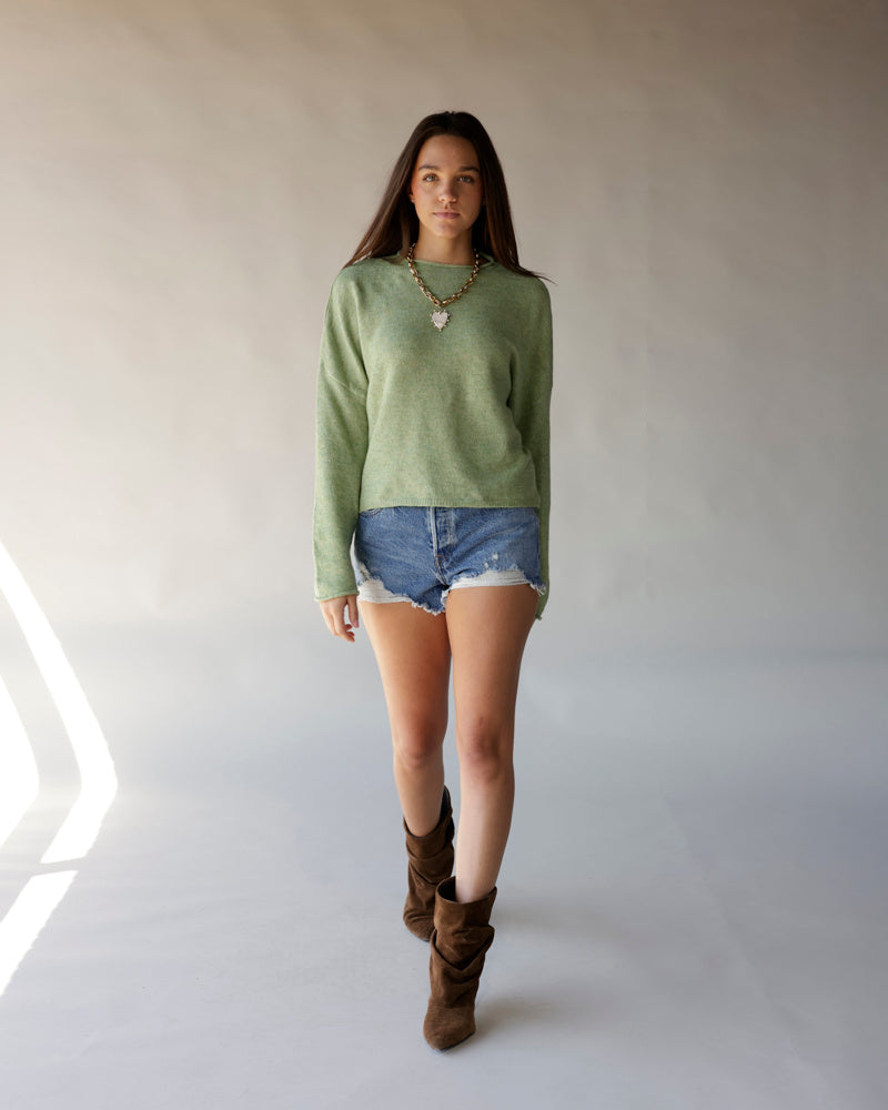Sage green mock neck long sleeve sweater styled with denim cutoff shorts and brown boots