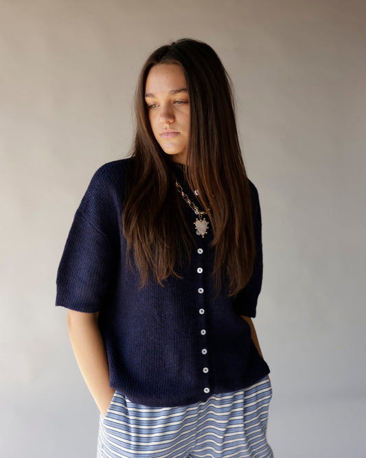 Navy blue short sleeve knit cardigan with white buttons, worn over striped pants