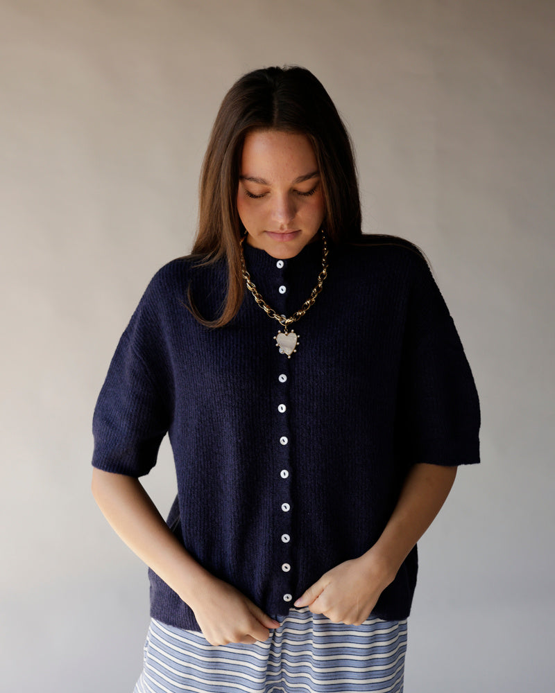 Navy blue short sleeve knit cardigan with white buttons, worn with striped skirt