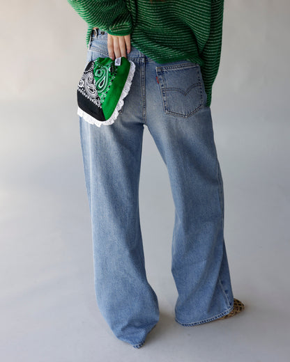 Green and black paisley bandana bag with white ruffled hem, held at hip