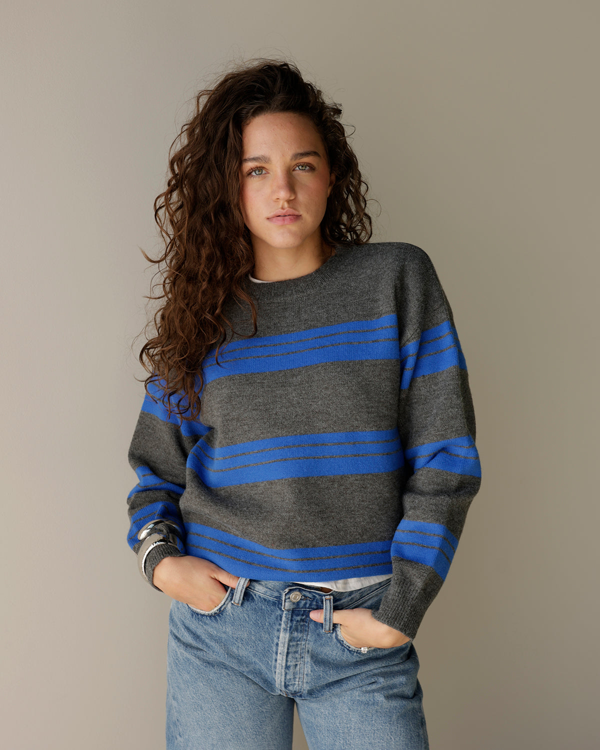 woman wearing a maude charcoal gray crewneck sweater with bold cobalt blue horizontal stripes, dropped shoulders and a relaxed fit, styled with light-wash denim.