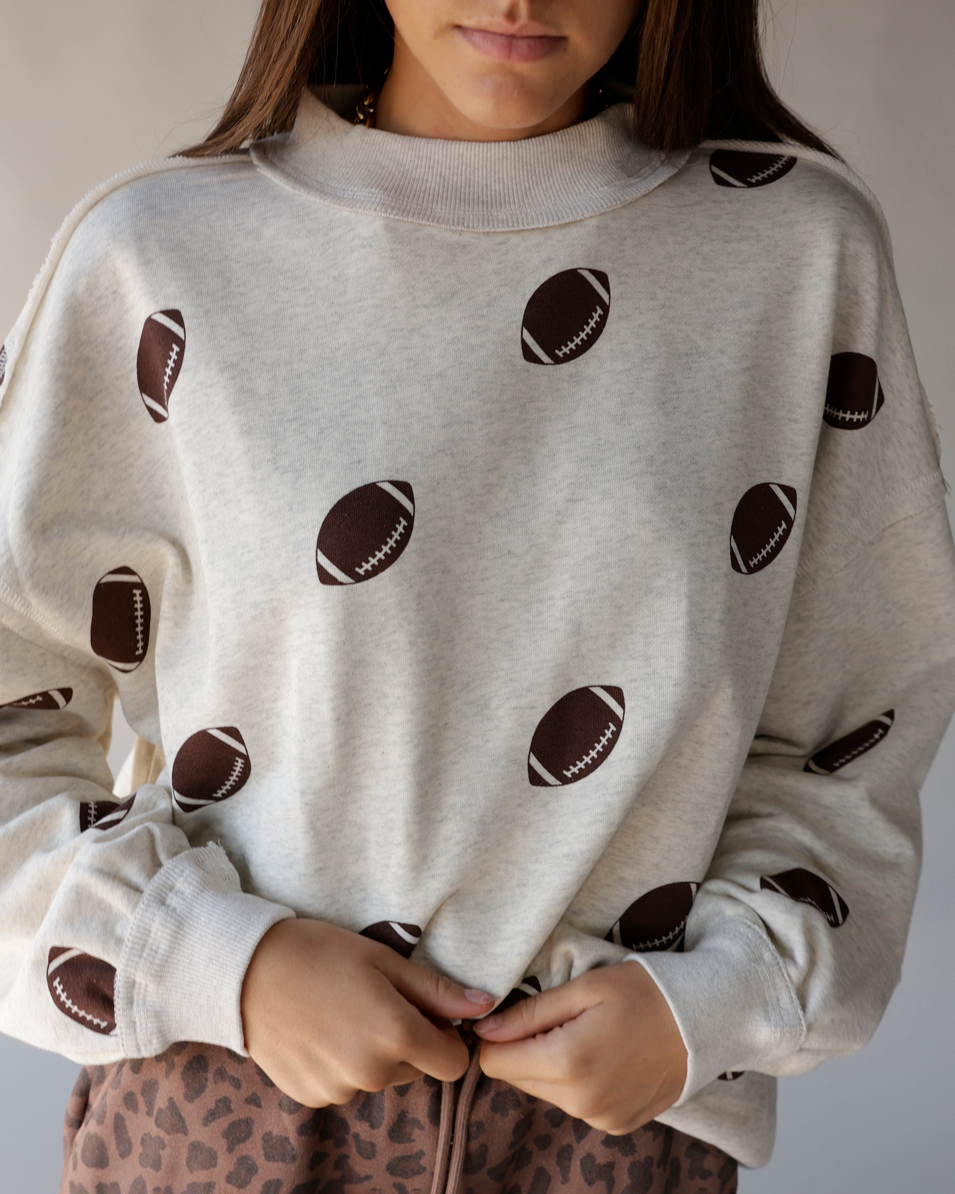 Cream mock neck sweatshirt with all-over dark brown football print pattern