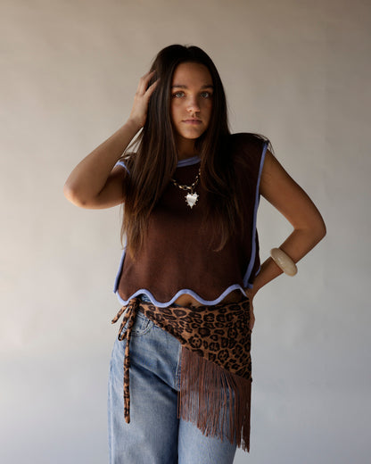 Brown sleeveless knit vest with lavender trim worn over blue jeans with leopard fringe belt
