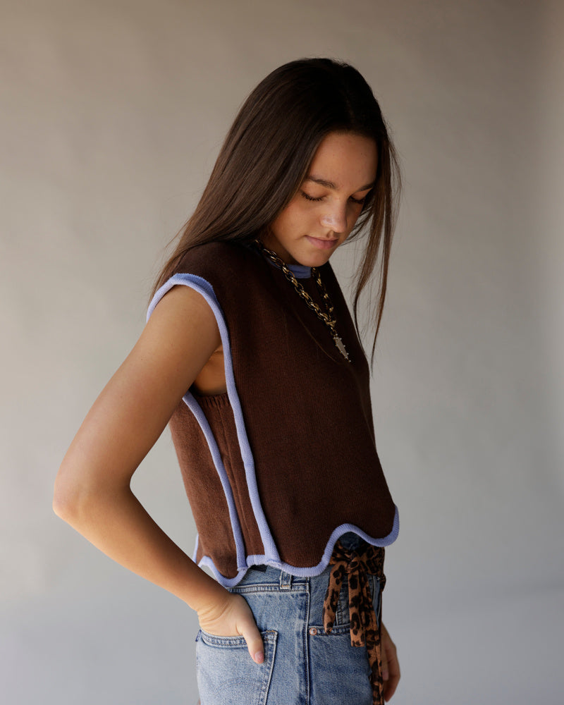 Brown cropped knit vest with lavender trim worn over blue jeans