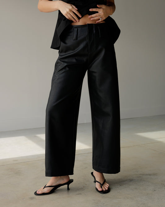 woman wearing maude black faux leather-look wide-leg pants with a structured waistband and relaxed silhouette, styled with black kitten heel sandals.