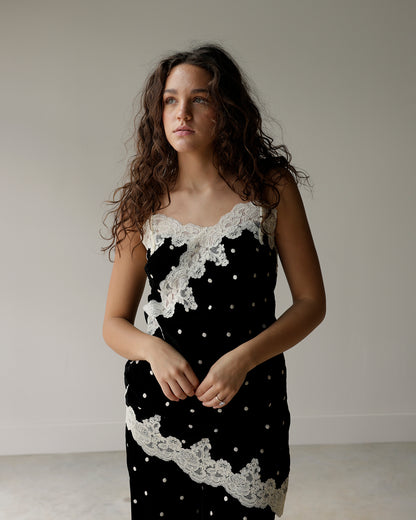woman wearing a maude black and ivory polka dot camisole top featuring floral lace appliqués, scalloped neckline and asymmetrical lace hem.