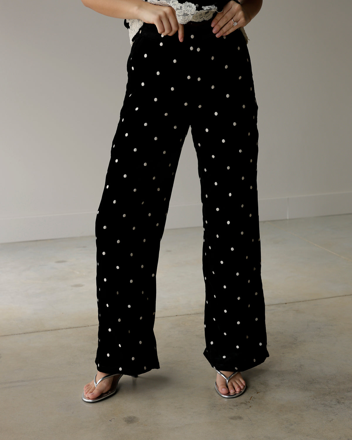 woman wearing maude black wide-leg pants with scattered ivory polka dots, styled with a lace-trimmed top and metallic silver sandals.