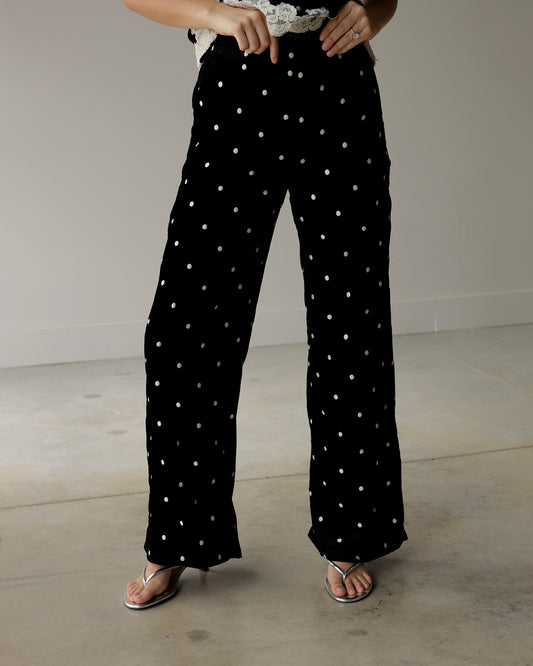woman wearing maude black wide-leg pants with scattered ivory polka dots, styled with a lace-trimmed top and metallic silver sandals.