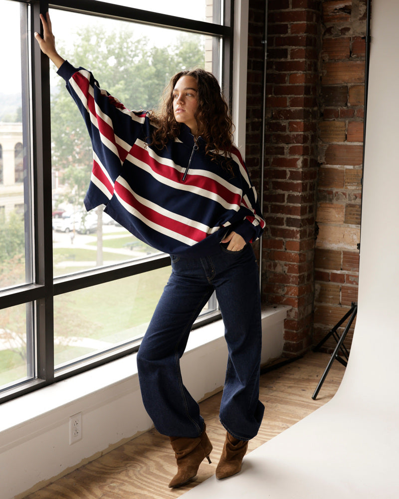 Navy, red, and white stripe quarter-zip pullover worn with dark jeans and brown boots.