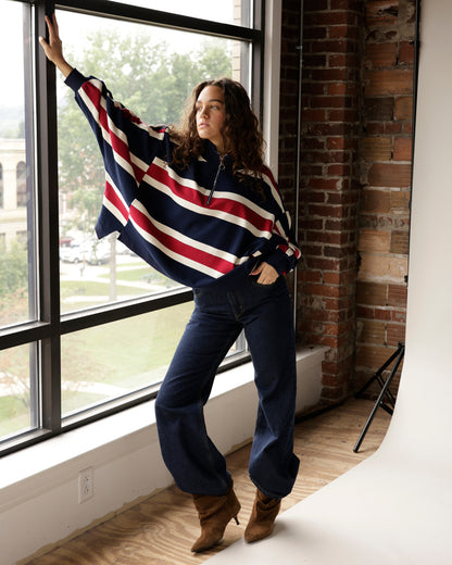 Navy, red, and white stripe quarter-zip pullover worn with dark jeans and brown boots.