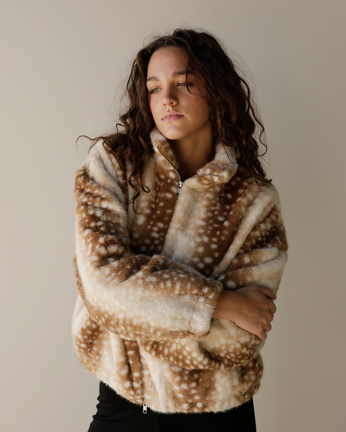 A woman wearing a brown and cream faux fur fleece pullover with a white spotted deer-like pattern, posed against a neutral beige background.