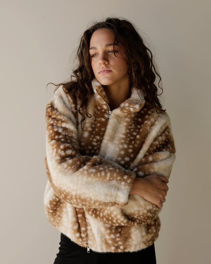 A woman wearing a brown and cream faux fur fleece pullover with a white spotted deer-like pattern, posed against a neutral beige background.