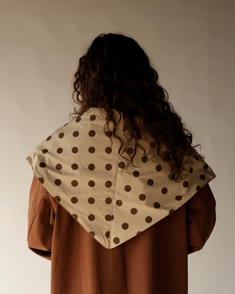Cream polka dot oversized scarf draped over rust brown trench coat, back view