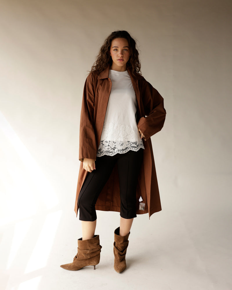 Oversized brown trench coat worn open over white lace-hem top and black pants