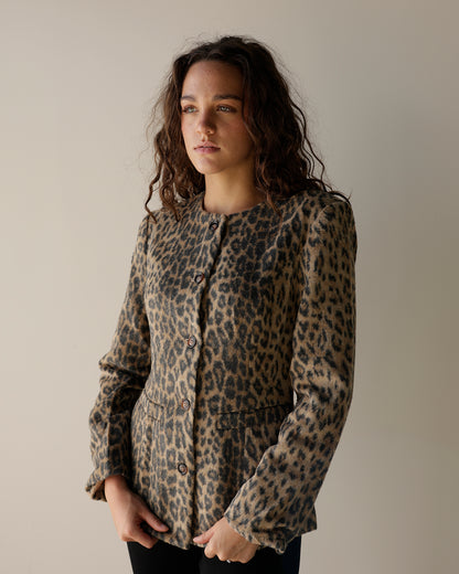 A woman wearing a leopard print button-up jacket, standing against a plain beige studio background.