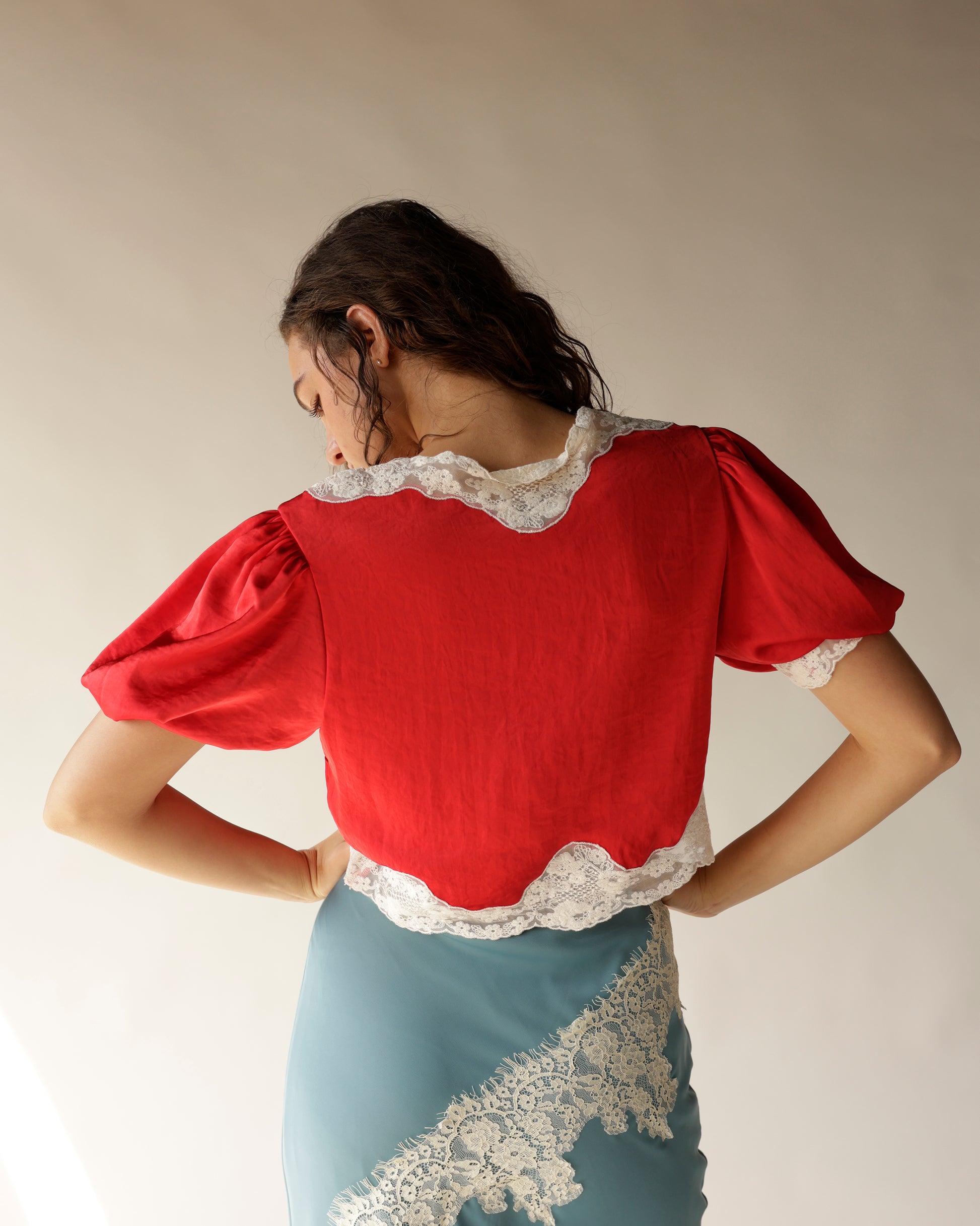 Red satin crop top with white lace trim and puff sleeves, back view