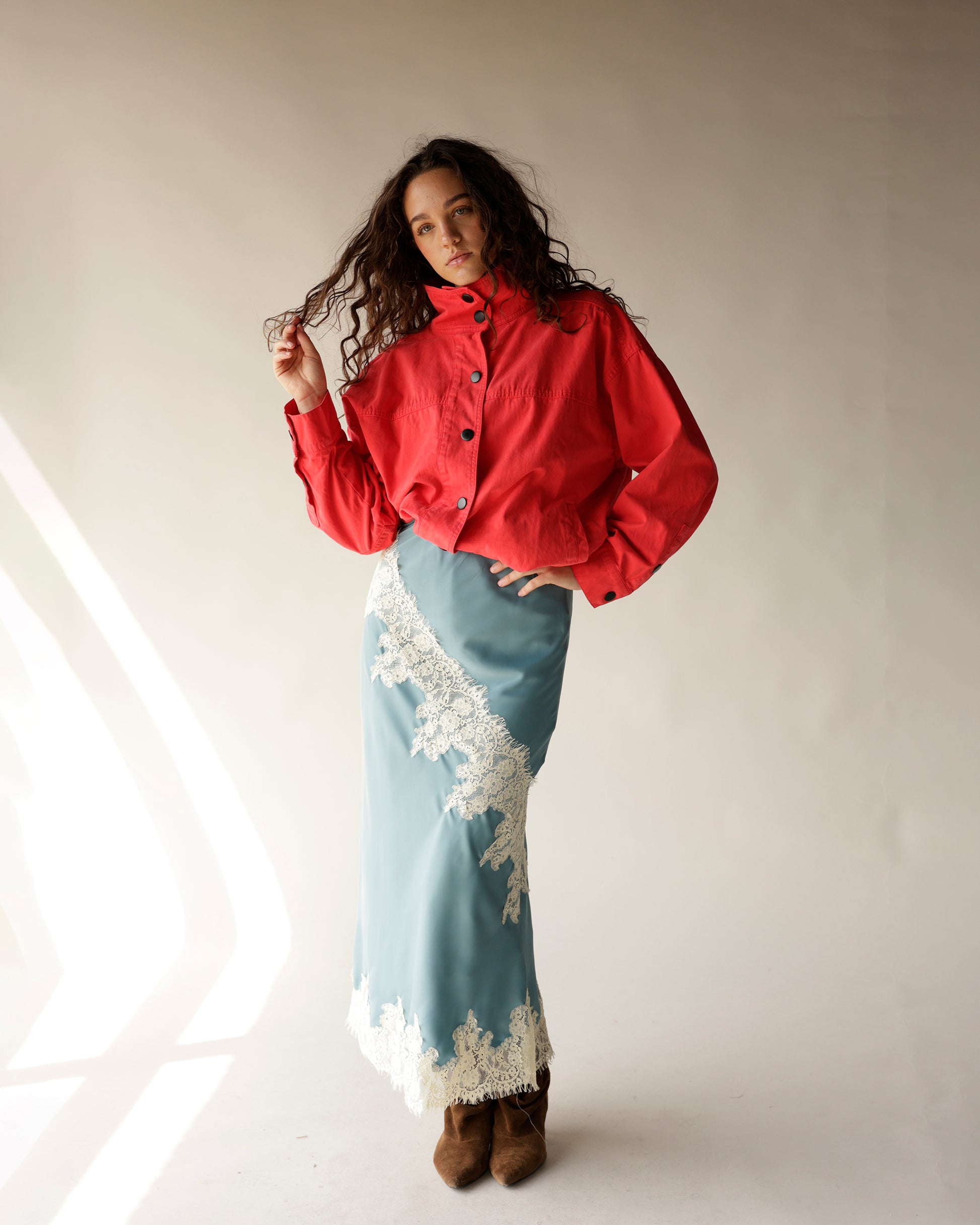 Dusty blue satin midi skirt with white lace trim, styled with red jacket and brown boots.