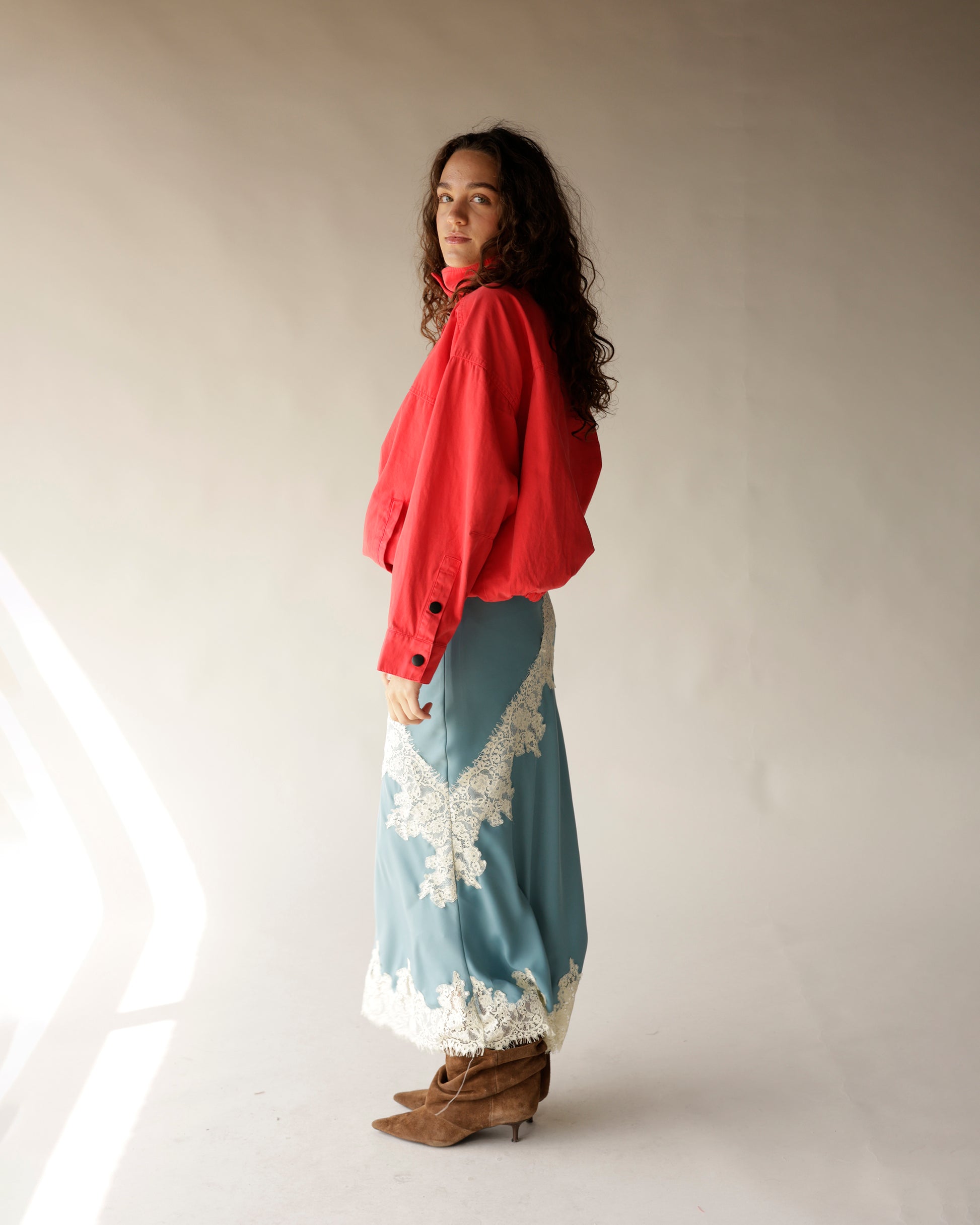 Dusty blue satin midi skirt with white lace trim detailing, styled with red jacket