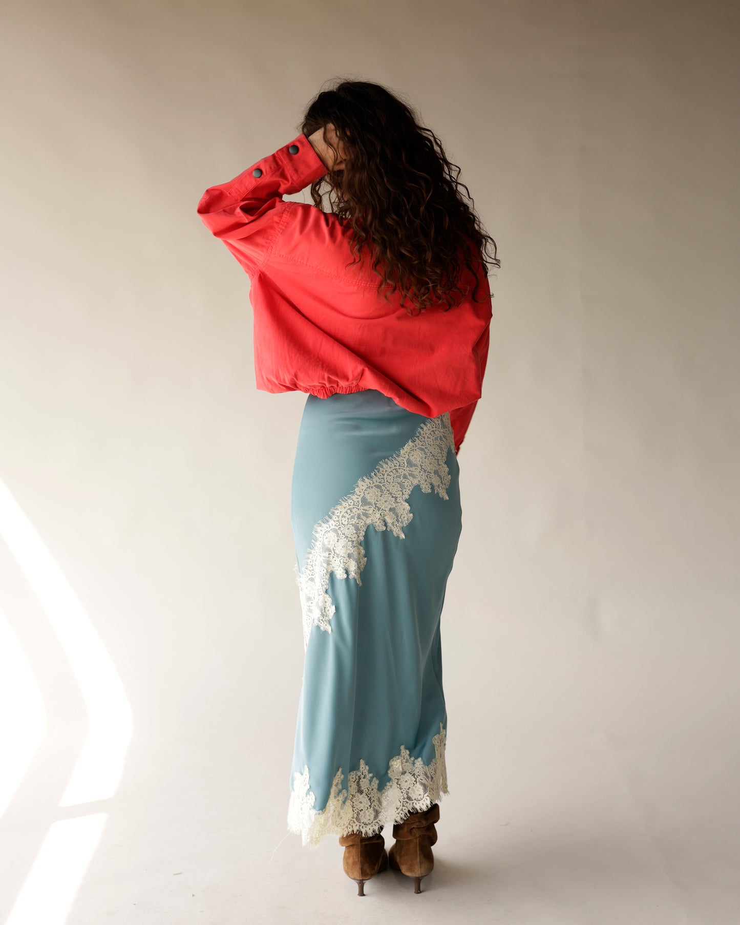 Dusty blue satin midi skirt with white lace trim detail, worn with red jacket