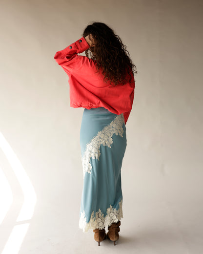 Dusty blue satin midi skirt with white lace trim detail, worn with red jacket