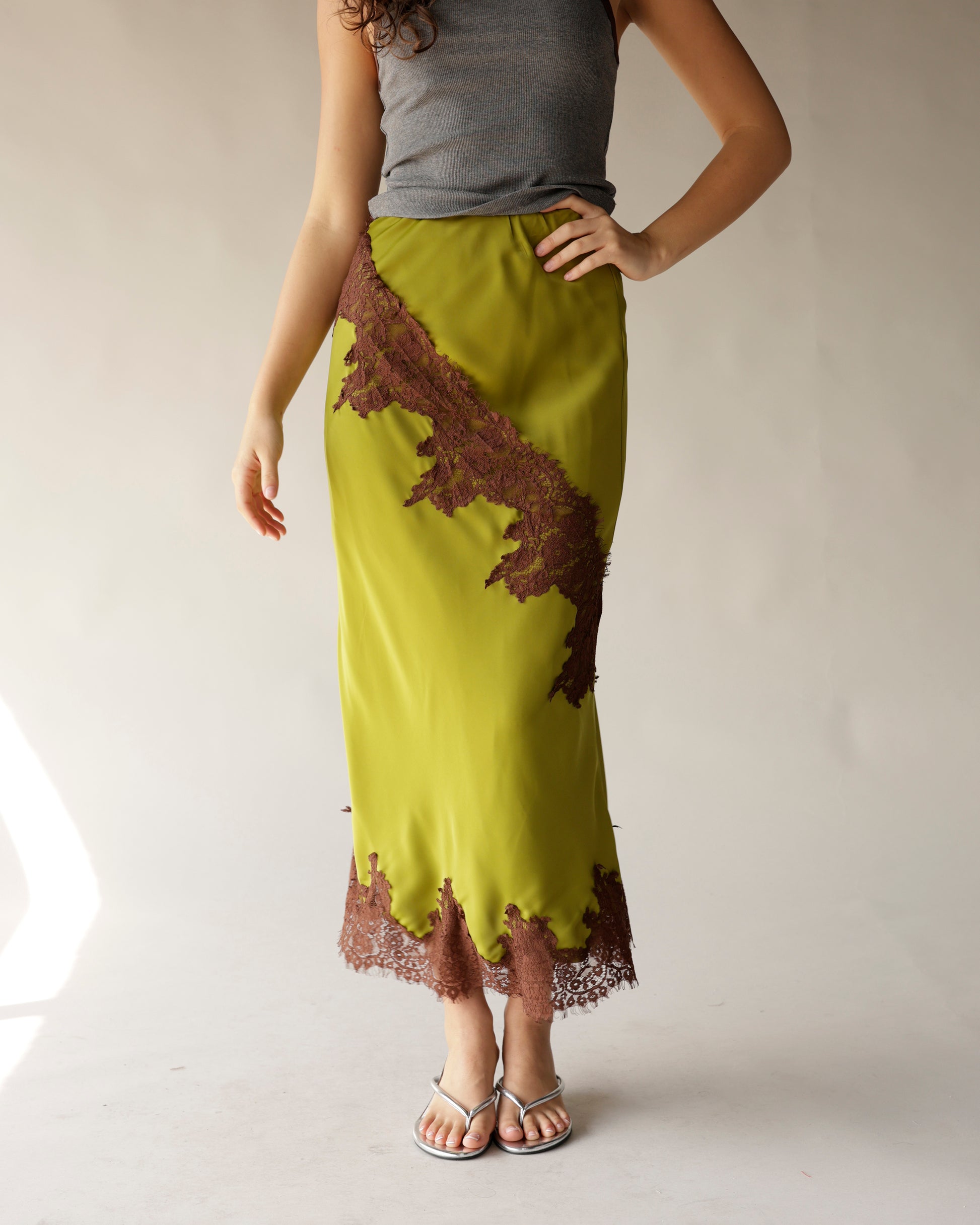 Exude vintage charm in this olive green, satin midi skirt with a diagonal brown lace appliqué and scalloped hem. Perfect for any occasion.