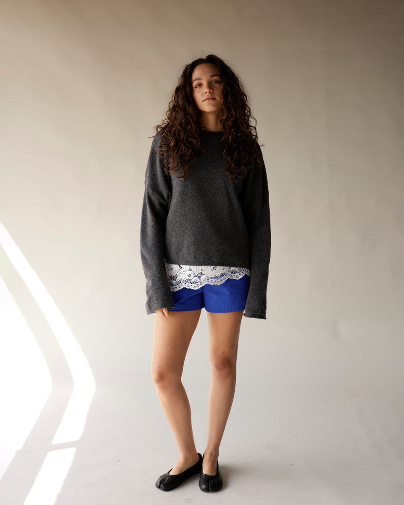 Bright blue track shorts with white lace trim, styled with grey oversized sweater and black flats