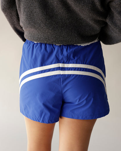 Blue athletic track shorts with double white stripes, elastic waistband, back view