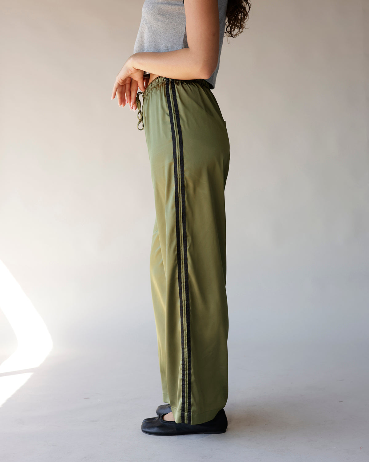 Olive green satin wide-leg track pants with black side stripe and drawstring waist