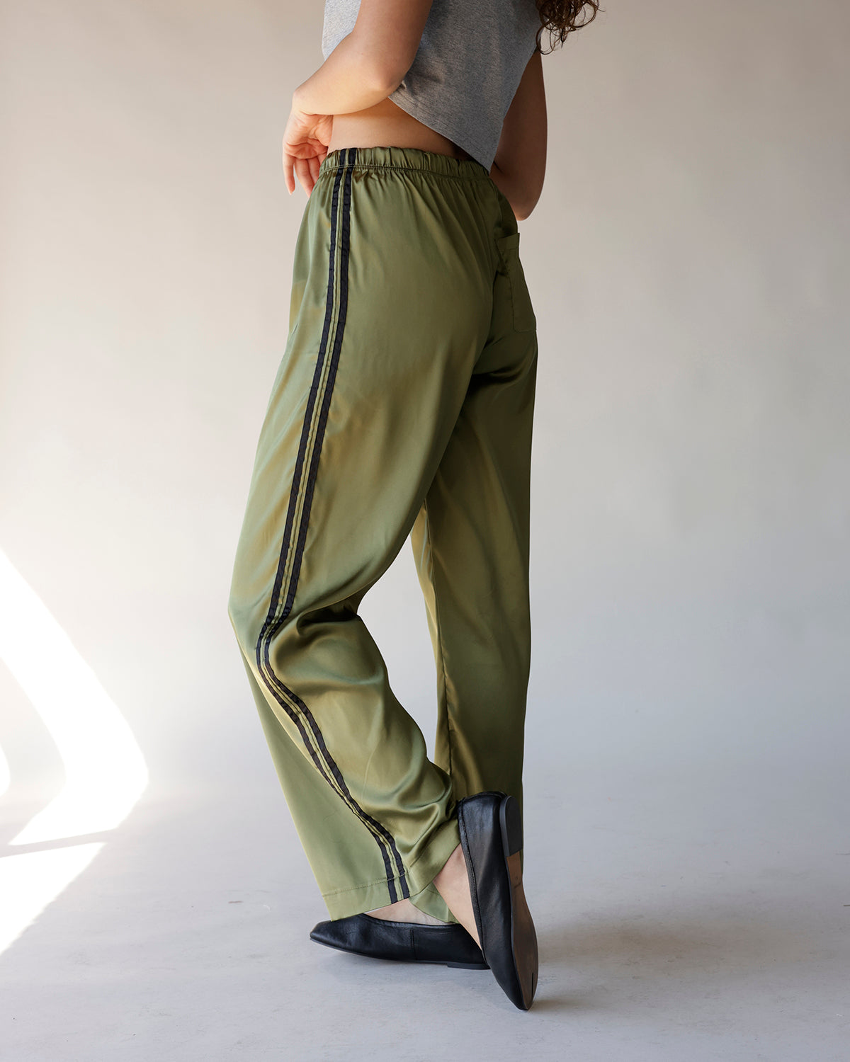 Olive green satin track pants with black side stripes and elastic waistband