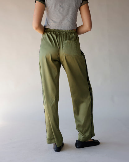 Olive green satin track pants with black side stripe and elastic waistband, back view