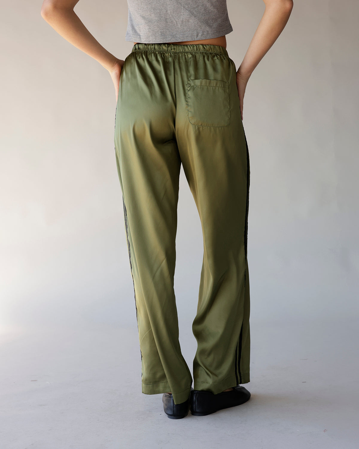 Olive green satin track pants with black side stripes and elastic waist, back view