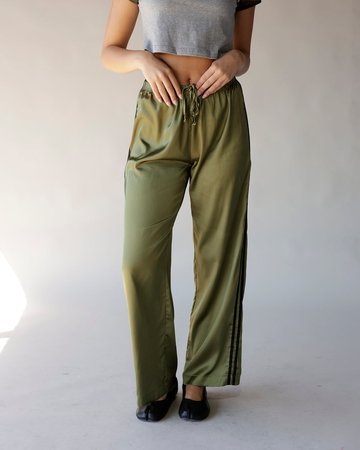 Olive green satin wide-leg track pants with black side stripes and drawstring waist