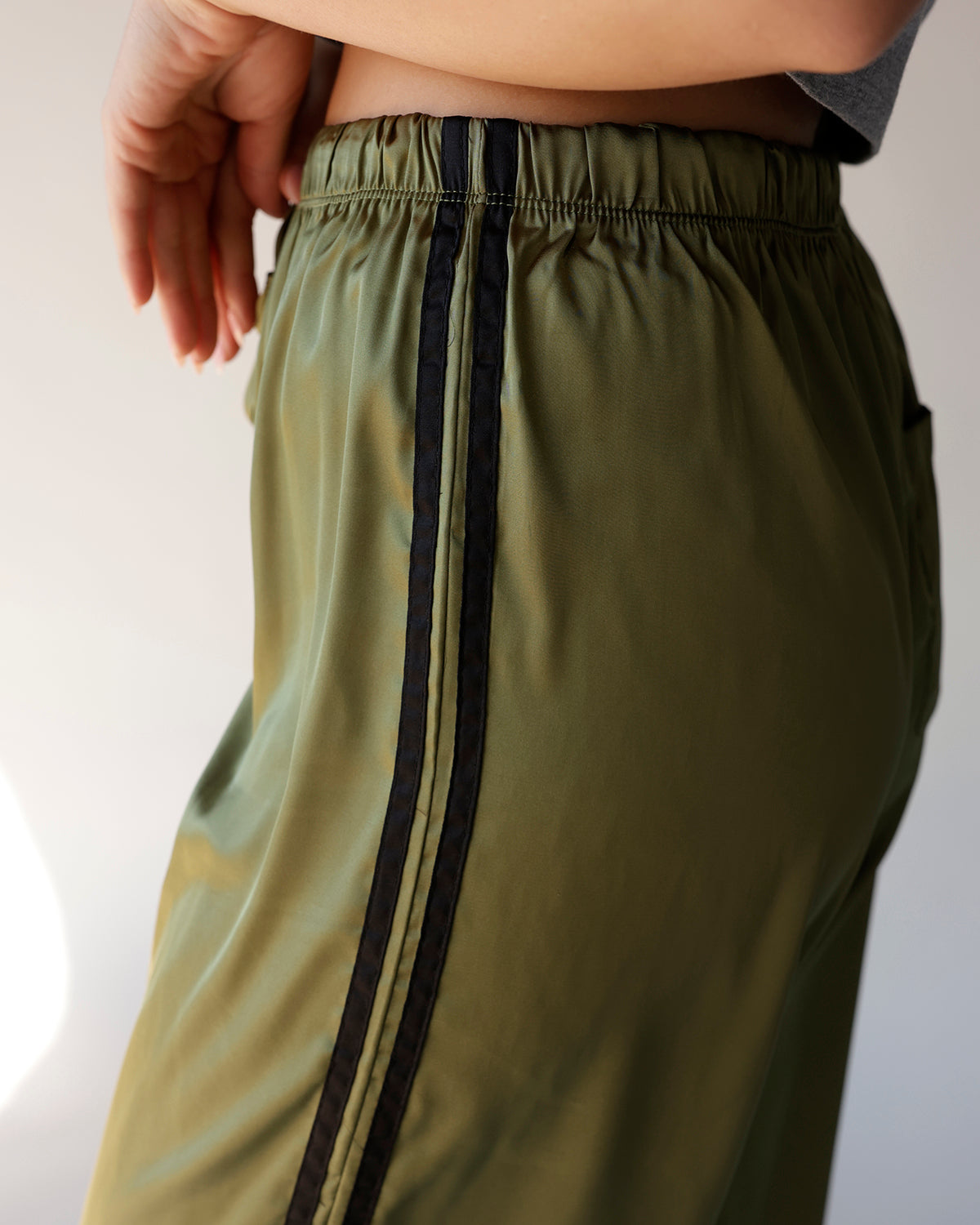 Olive green satin track pants with black side stripe and elastic waistband