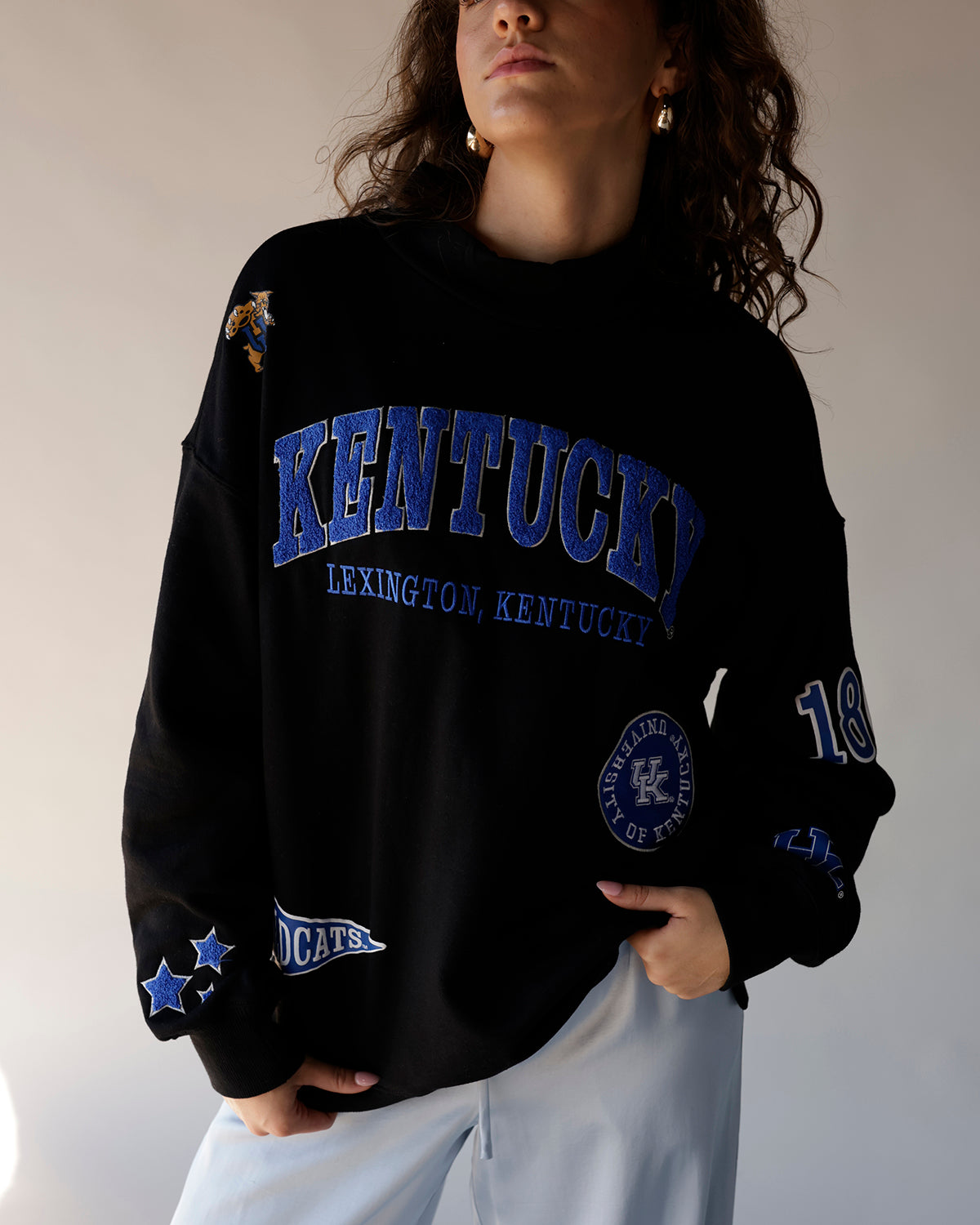 Black Kentucky Wildcats crewneck sweatshirt with blue varsity text and multi-patch graphics