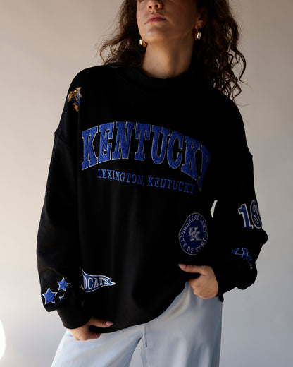 Black Kentucky Wildcats crewneck sweatshirt with blue varsity text and multi-patch graphics