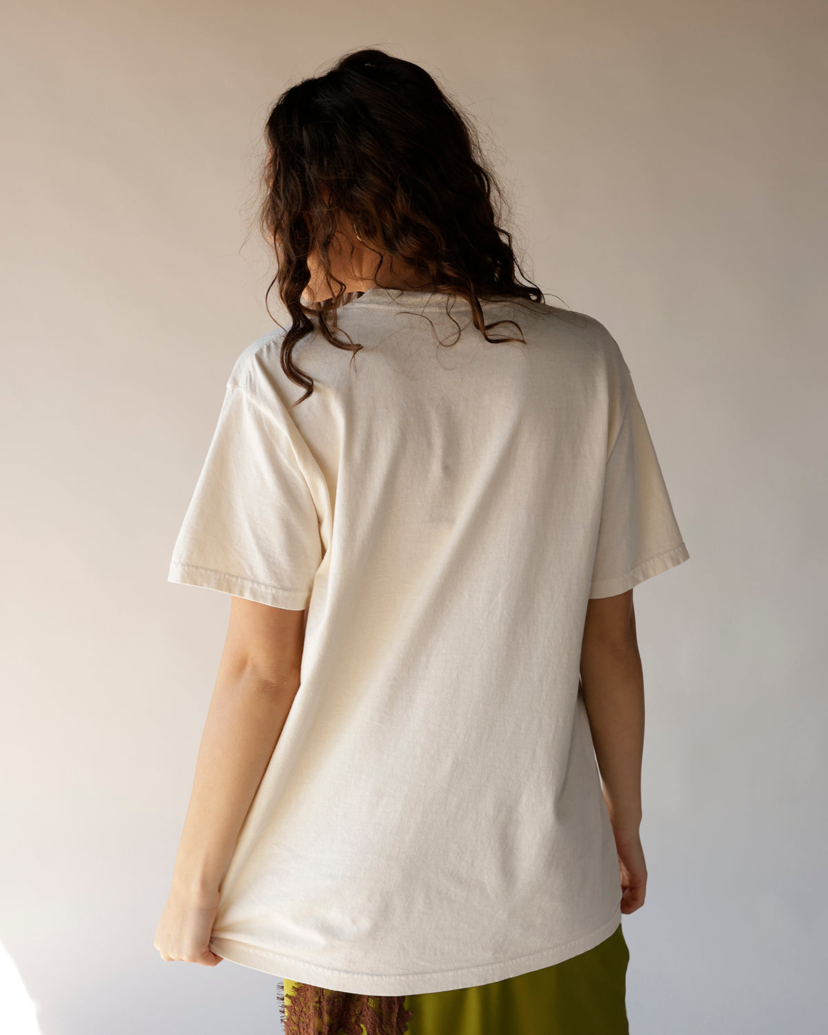 Cream oversized graphic tee shown from back, paired with olive green bottoms
