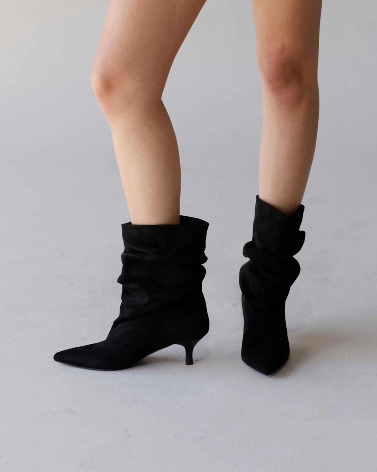 Black suede slouch ankle booties with kitten heel and pointed toe on model